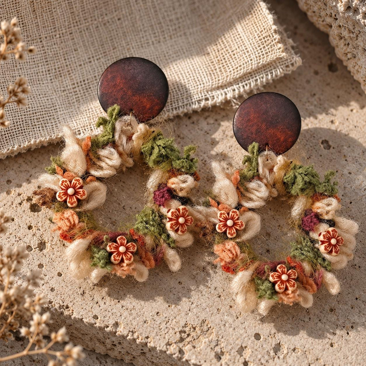 Angled view of the yarn floral-wreath earrings on textured cream stone.