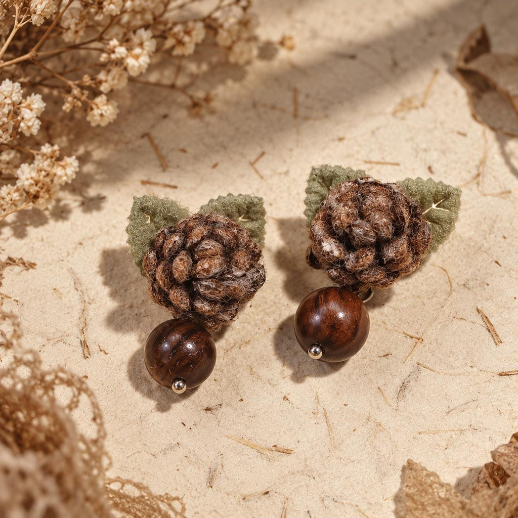Angled view of Hazelwood brown crochet-flower earrings with green leaves on cream stone.