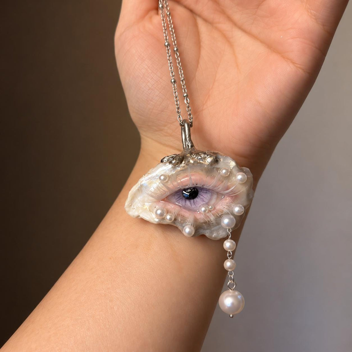 Lilac Veil oyster-eye pendant hanging from a chain over a wrist.